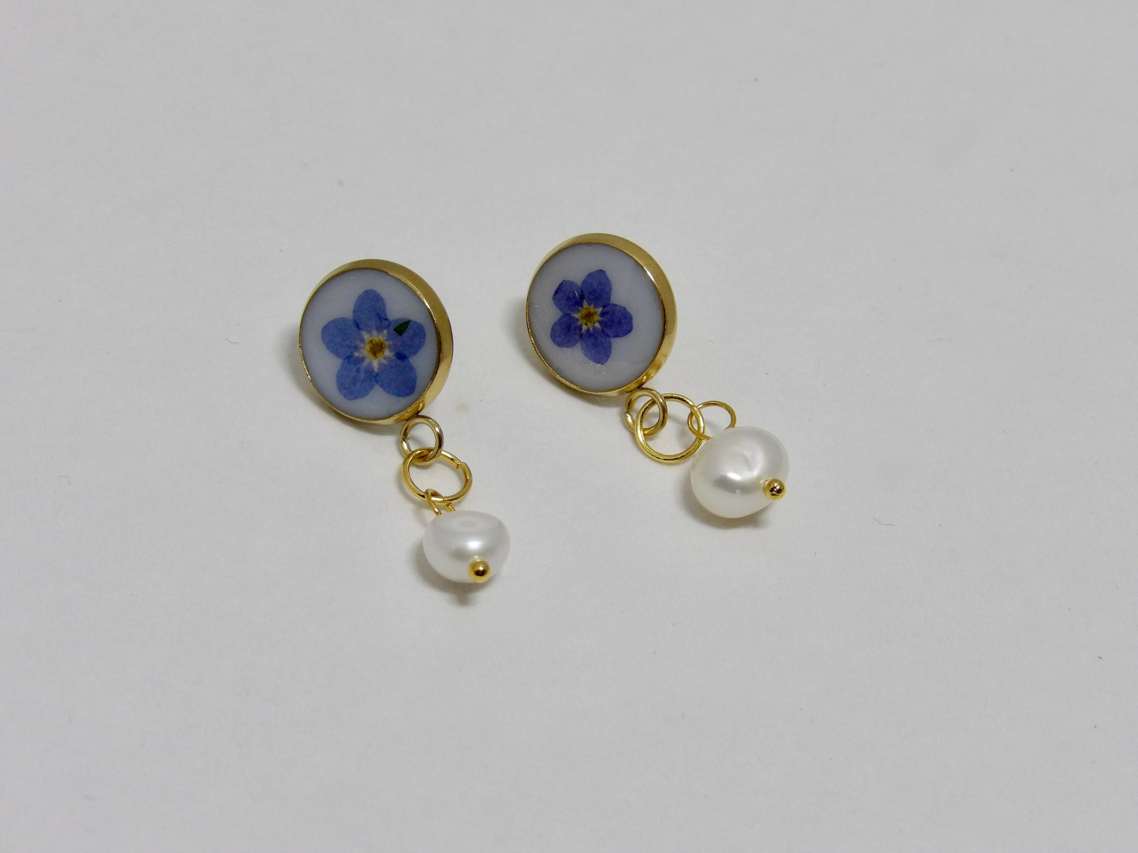 Pair of earrings with blue flower and pearl design on a white background